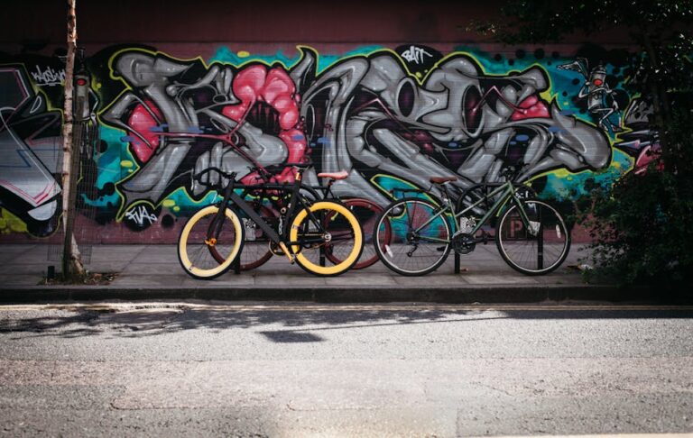 Two bicycles parked against a vibrant graffiti wall on a sunny day, adding urban flair.