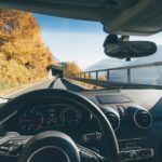 View from car interior driving through a scenic mountain road with autumn foliage and clear skies.