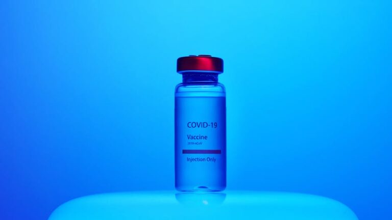 Vial of COVID-19 vaccine labeled for injection, set against a blue background.