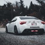 White sporty car parked on a quiet scenic forest road, showcasing sleek design and quiet surroundings.