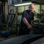 Bald mechanic focused on repairing a car engine in a garage setting.