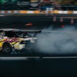 Dynamic image of a car drifting on a racing track with smoke trailing behind.