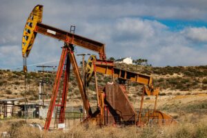A rusty oil pumpjack situated in a desert-like landscape under a partly cloudy sky.