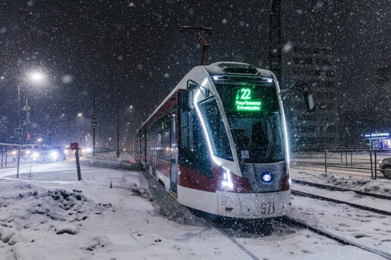 A tram navigates through a snowy cityscape at night, illuminated by streetlights.
