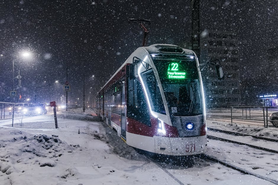 A tram navigates through a snowy cityscape at night, illuminated by streetlights.