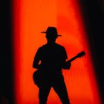 A dramatic silhouette of a guitarist on a stage with vibrant red lighting.