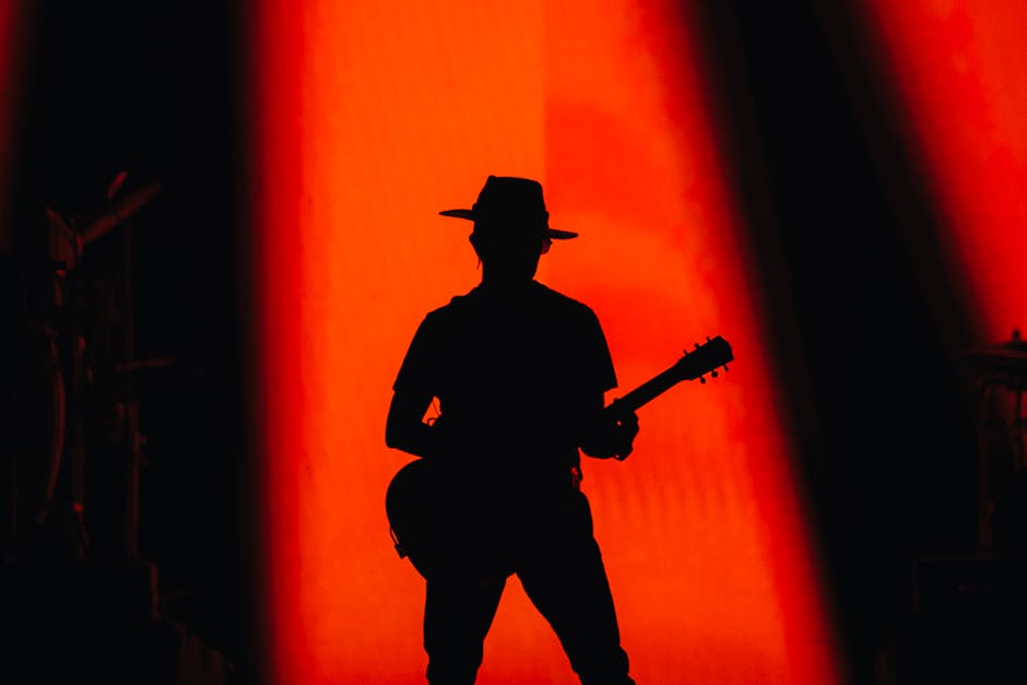 A dramatic silhouette of a guitarist on a stage with vibrant red lighting.