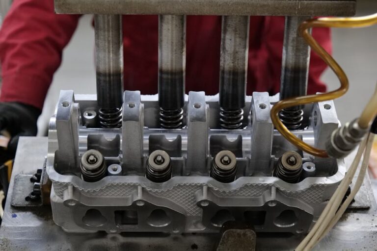 Detailed view of a metallic engine cylinder head with springs and pistons, assembled in an industrial workshop.