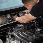 Mechanic fixing a car engine under the hood showing detailed components.