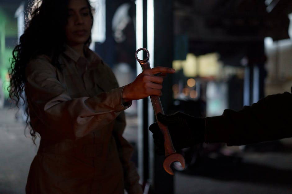 A mechanic handing over a wrench in a dimly lit garage workshop, creating a moody atmosphere.