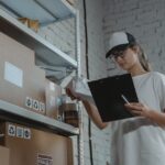 Warehouse worker organizing packages on shelf with clipboard.