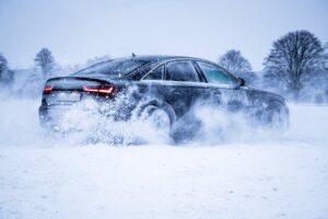A sleek black car powers through snow, creating a dynamic winter scene with swirling snowflakes.