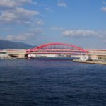 Bright red bridge over Kobe port under a clear autumn sky, showcasing modern architecture.