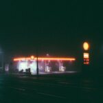 A foggy night scene of an illuminated gas station, featuring vibrant neon lights.