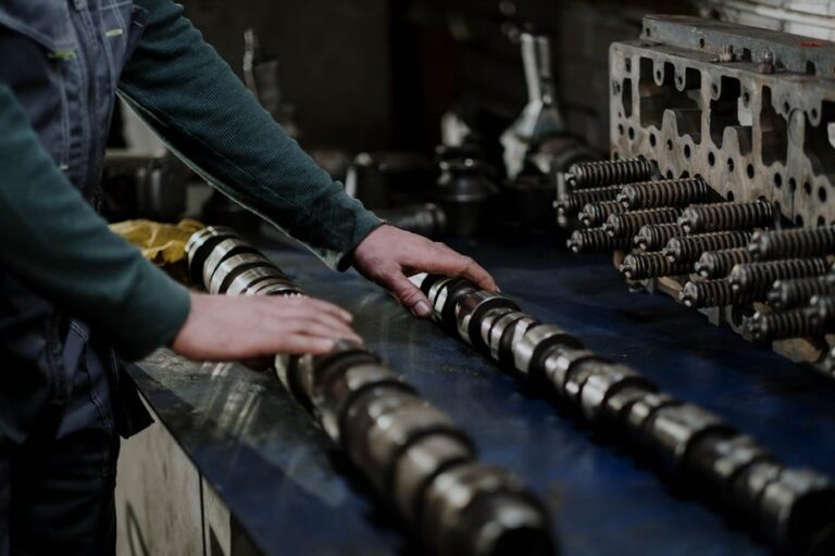 Worker handling camshafts and cylinder head in a mechanic workshop.