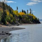 Vibrant autumn colors along the rocky shore of Yellowstone Lake under a clear sky.
