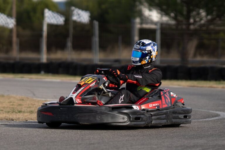 A person in full gear driving a go-kart on an outdoor racing track, captured in motion.