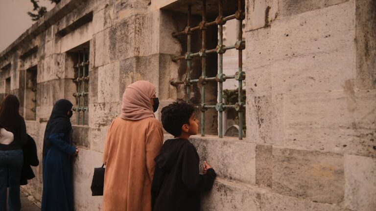 A group of people curiously observing a historical building with barred windows.