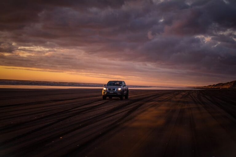 A 4x4 SUV driving on a sandy beach during a stunning sunset with dramatic clouds.