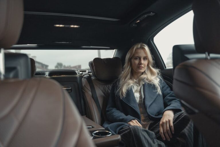 Elegant woman in a blue coat sitting in the back seat of a luxury car.