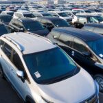 Modern sparkling clean new automobiles on asphalt parking near factory of manufacture in daytime