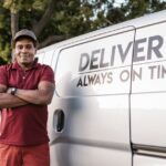 Delivery driver standing with arms crossed near a company van displaying a timely service slogan.