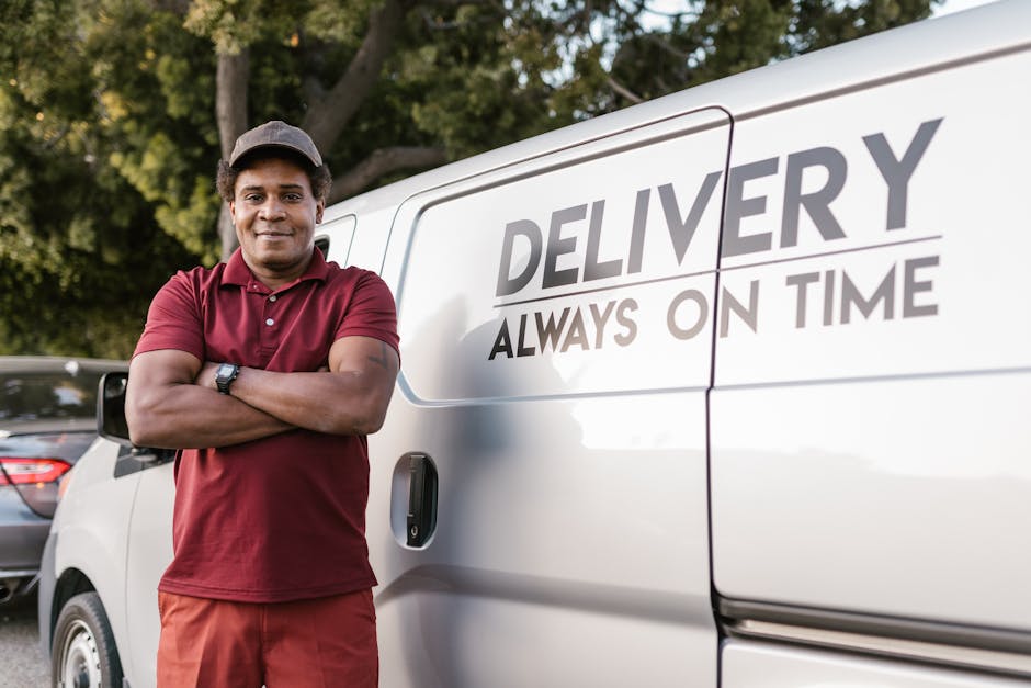 Delivery driver standing with arms crossed near a company van displaying a timely service slogan.
