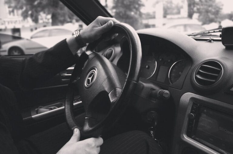 Detailed black and white photo inside a luxury car focusing on the steering wheel and driver's hands.