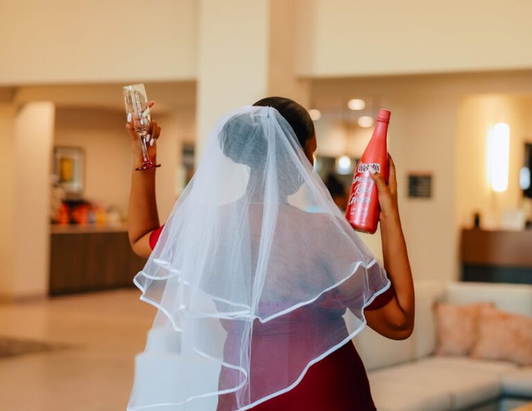 Bride in veil holding champagne glass and bottle, celebrating indoors.