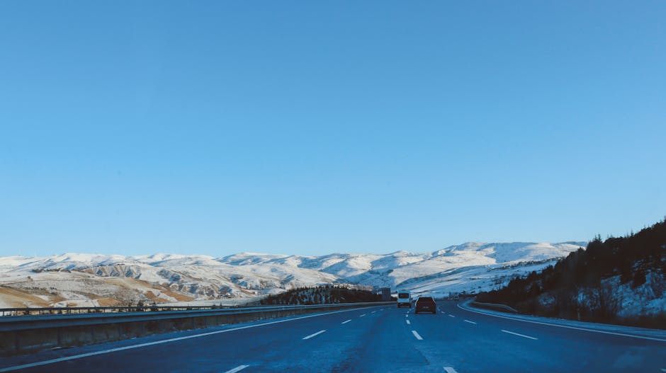 Scenic view of a highway leading through snowy mountains under a clear blue sky.